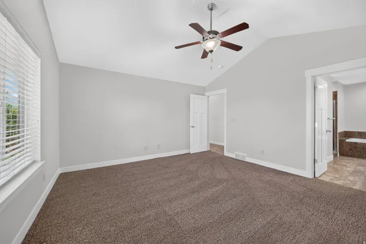 Vaulted ceiling with a ceiling fan, plush carpet flooring, white window blinds, and white interior doors