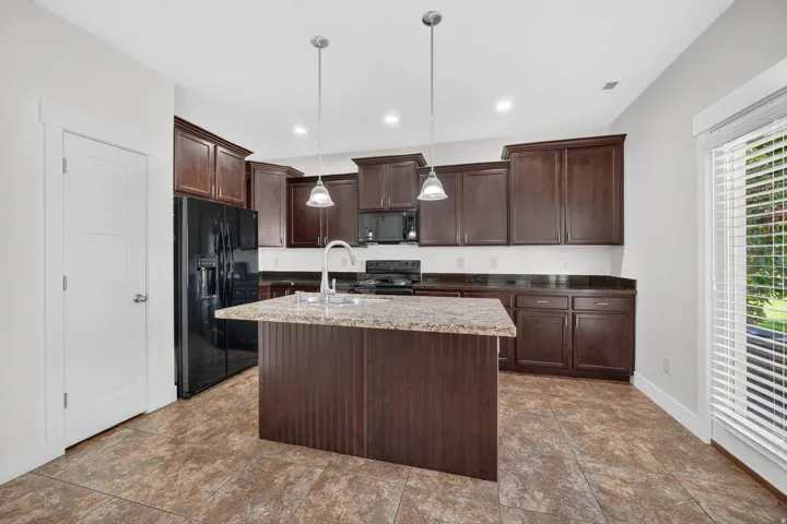 Kitchen featuring dark wood-finish cabinetry, black appliances, a central island with a stone-finish countertop, and pendant lighting