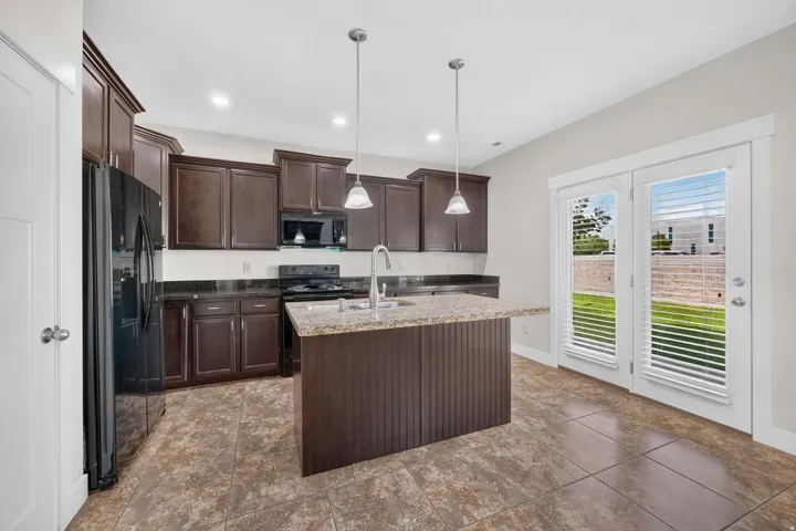 Dark wood-finish cabinetry with coordinating backsplash, central kitchen island with countertop, and double glass-paneled doors
