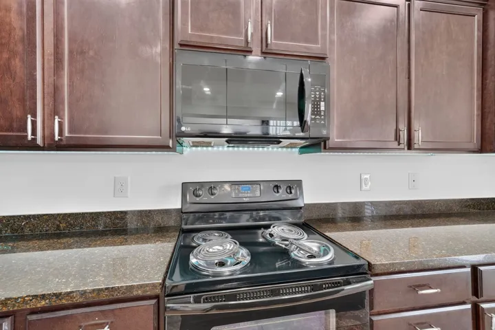 Dark wood cabinetry with brushed nickel hardware, black electric range with coil burners, and dark speckled countertops