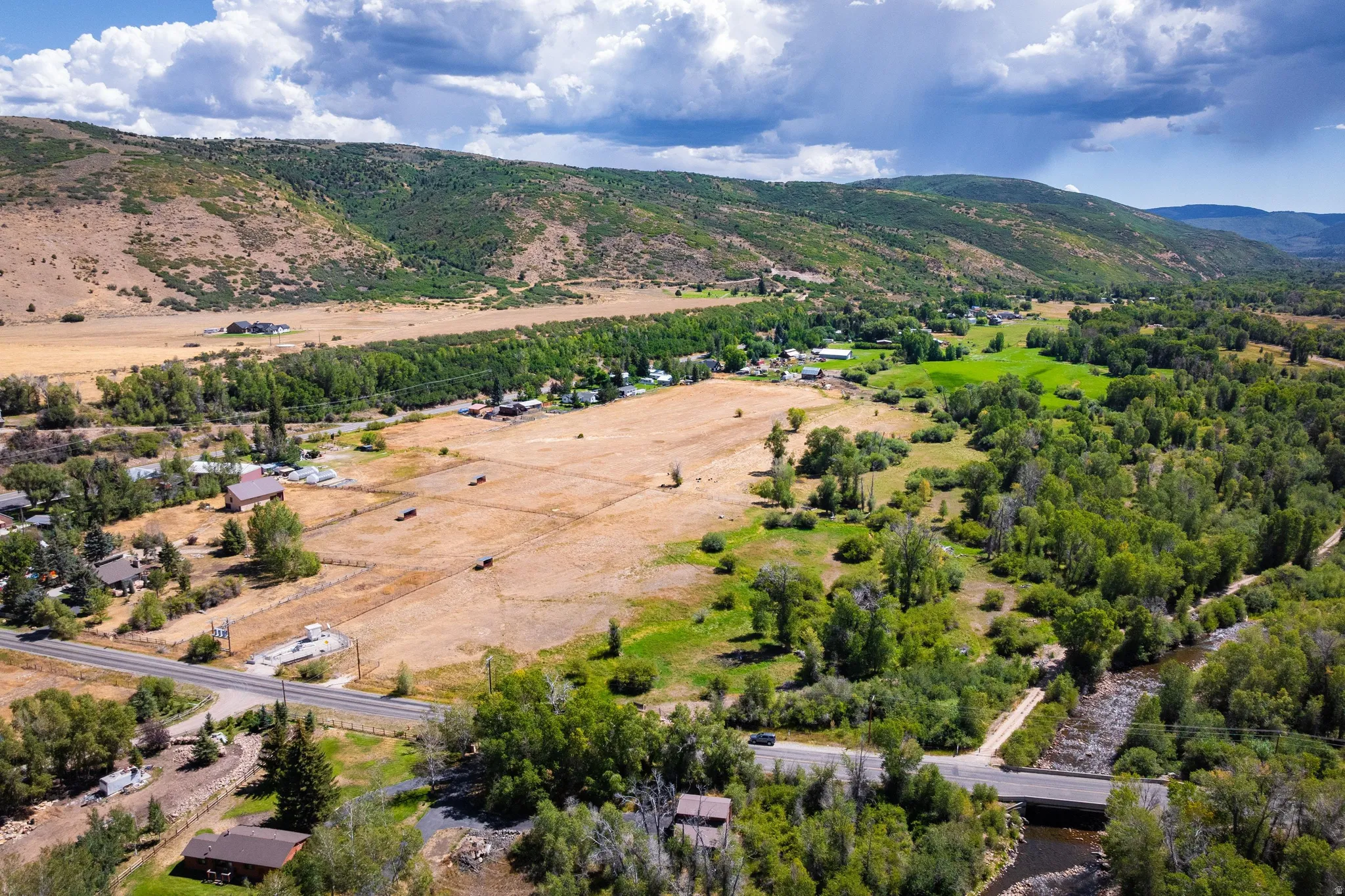 Expansive rural landscape featuring a river, mature trees, open fields, and distant mountains