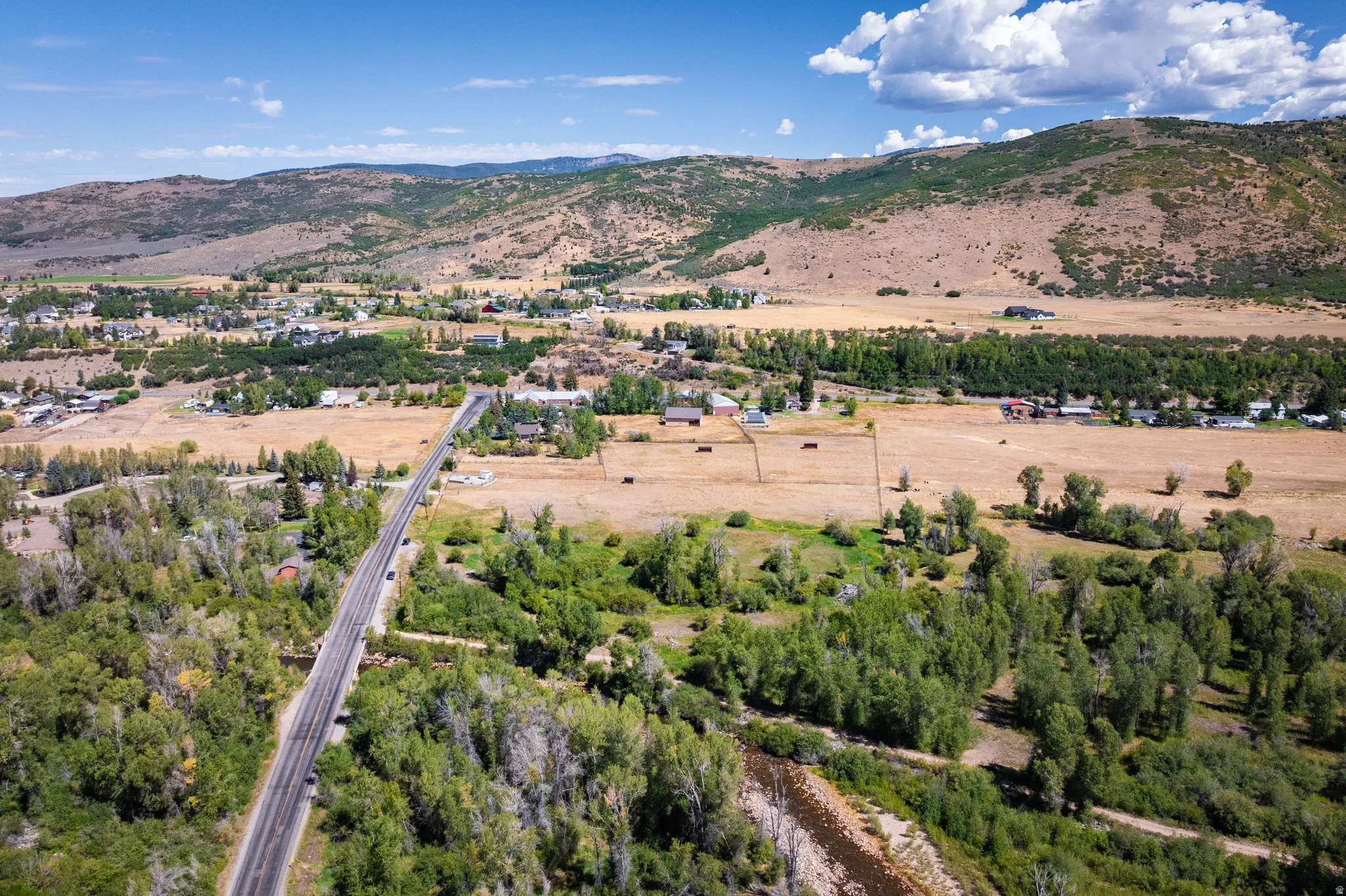 Expansive property featuring rural landscape, distant mountain backdrop, a prominent paved road, a river, and substantial mature trees