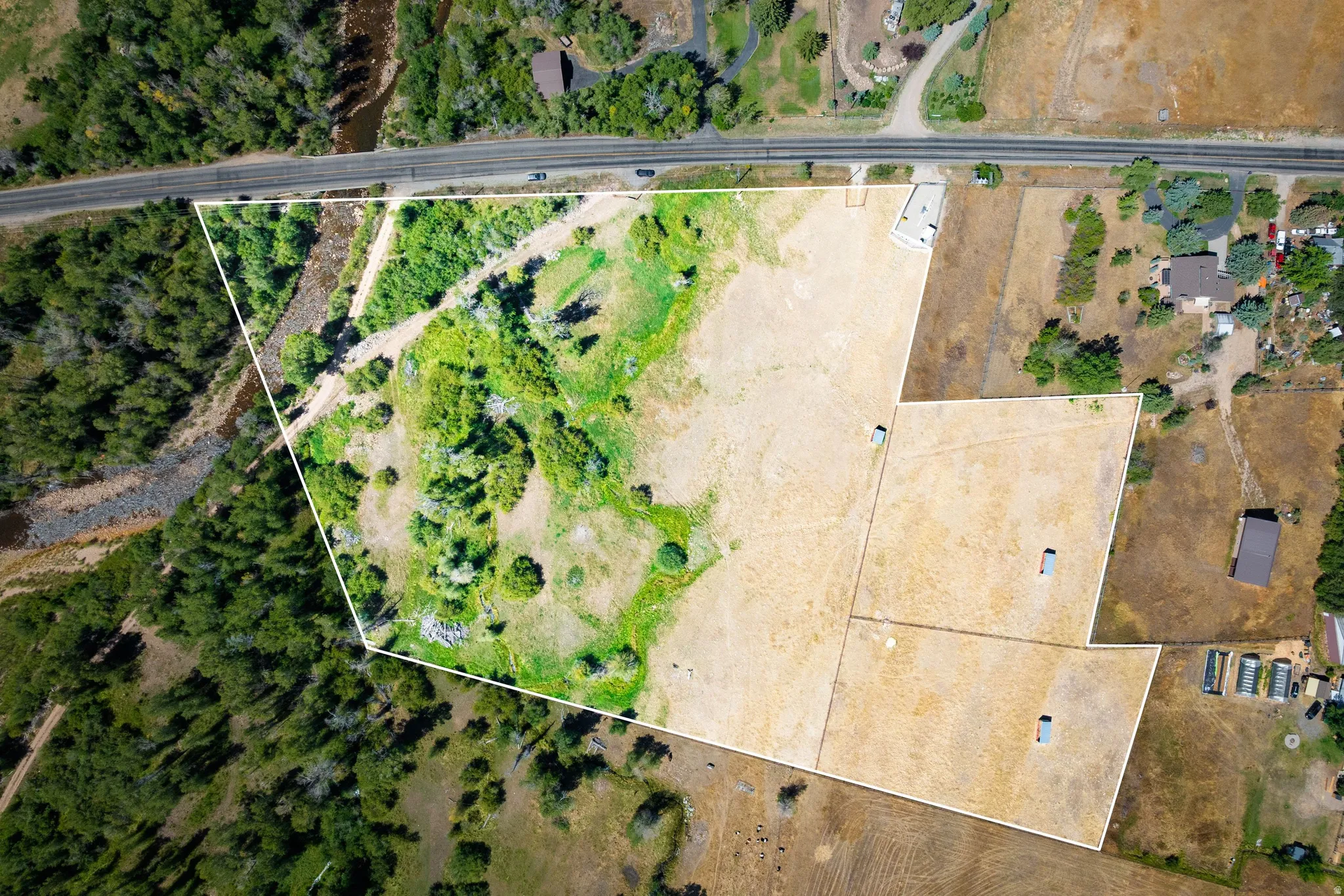 Expansive land parcel featuring diverse terrain, mature trees, open clearings, and a prominent road frontage