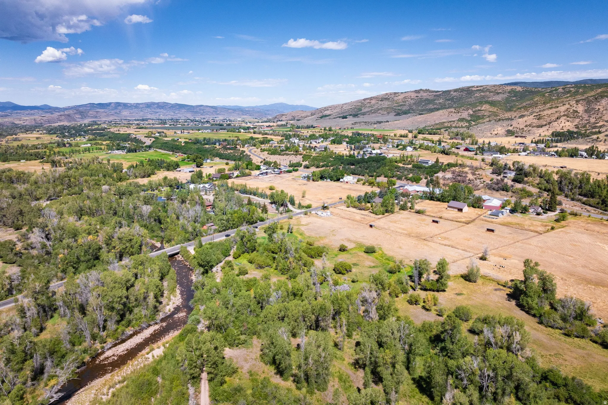 Expansive rural landscape with a winding river, mature tree coverage, scattered agricultural fields, and distant mountainous terrain