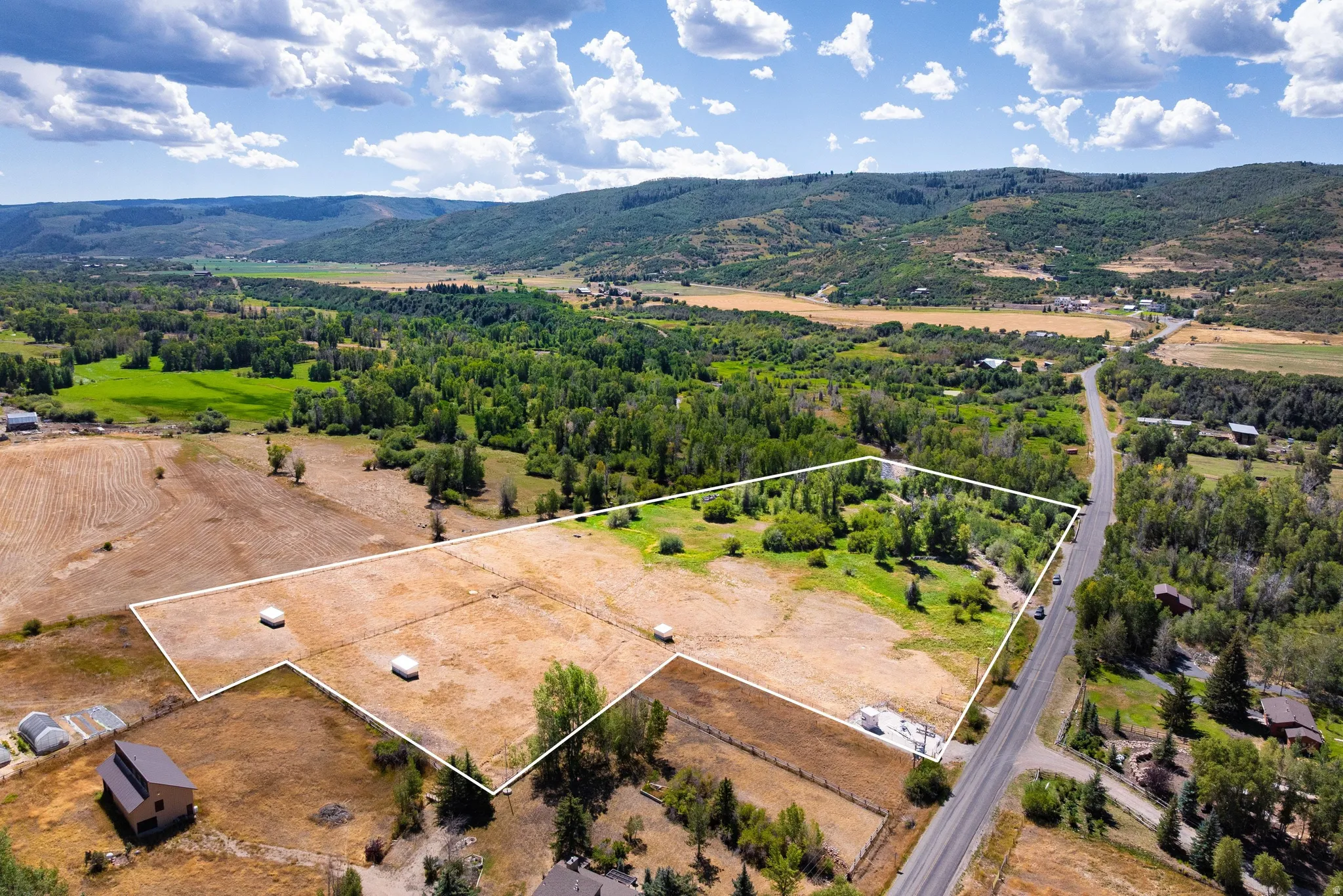 Expansive rural property featuring an open field, mature trees, and direct road frontage