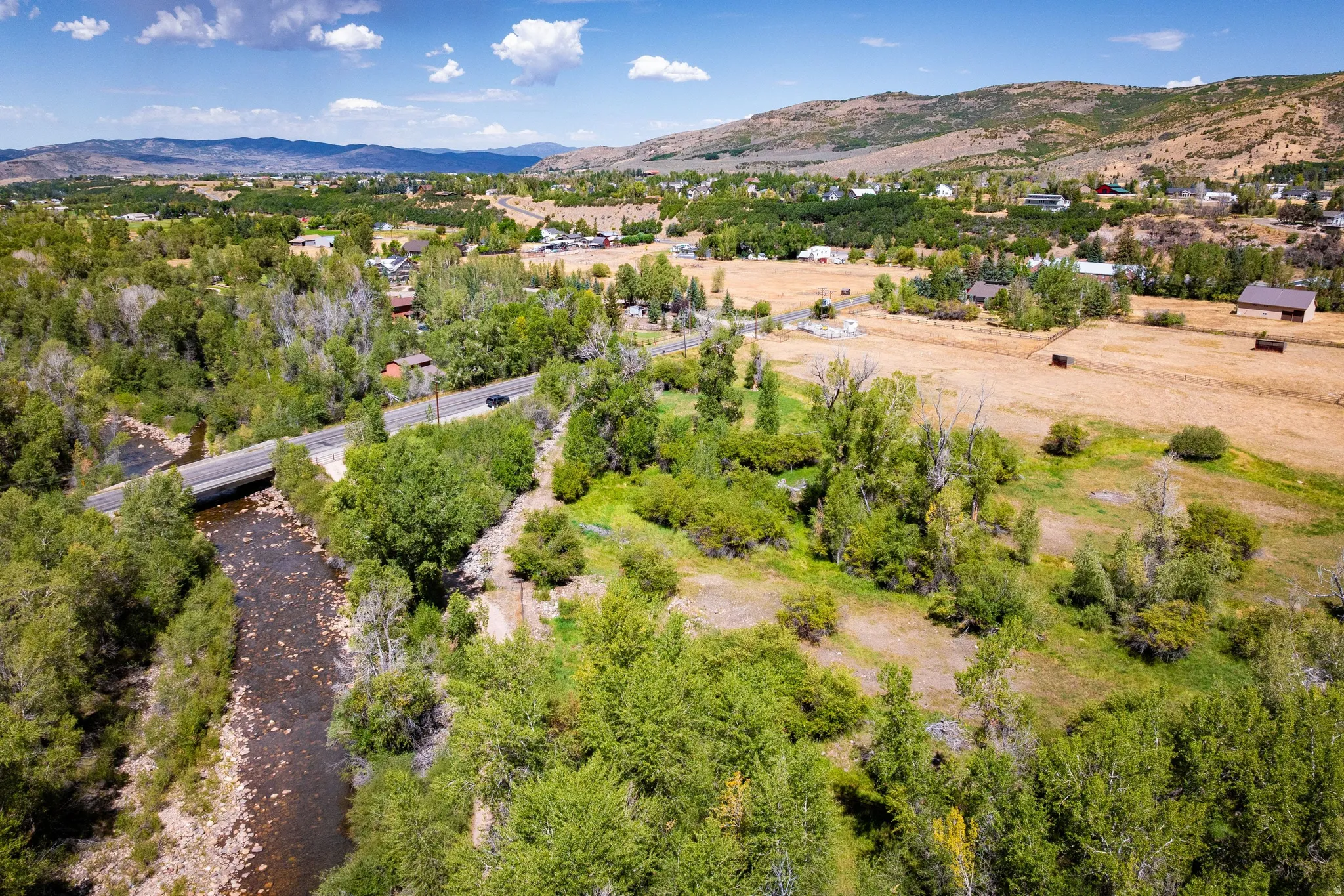 Expansive landscape featuring a natural river, mature trees, a paved road, and distant mountain ranges
