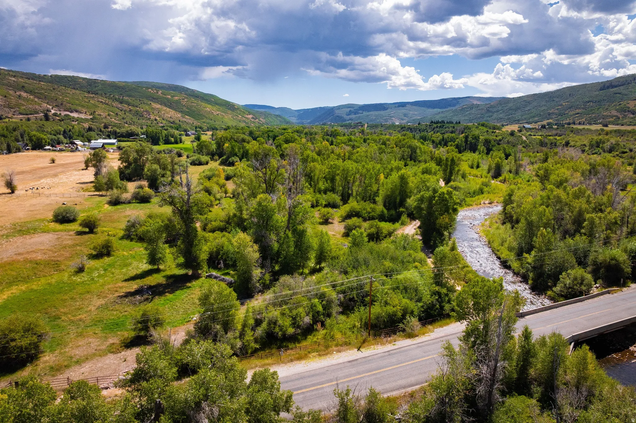 Expansive natural landscape featuring a winding river, mature trees, open fields, and distant hillsides