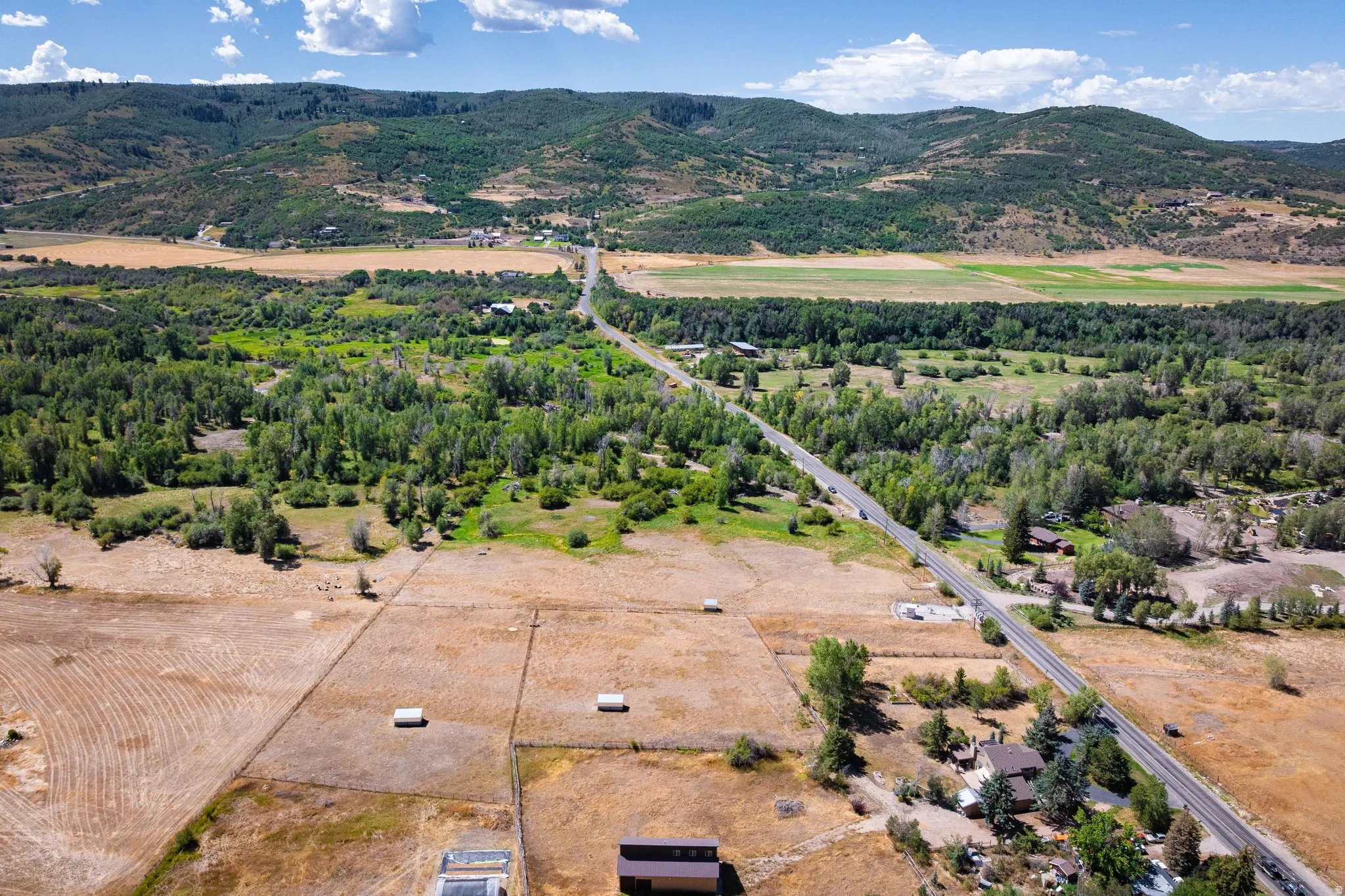 Expansive rural property featuring a paved road, mature trees, and mountainous topography