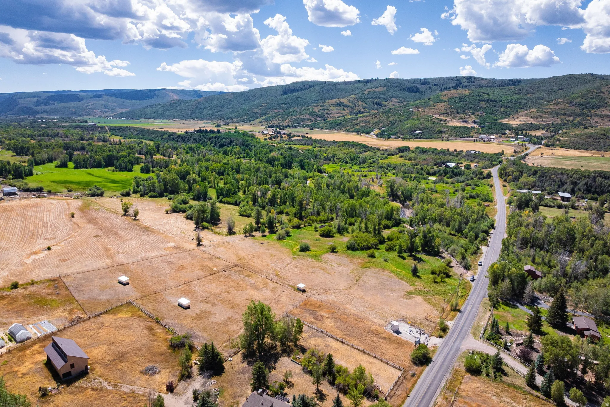 Expansive rural landscape featuring fenced parcels, verdant tree cover, and distant mountains
