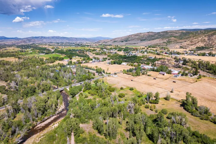 Expansive rural landscape with a winding river, mature tree coverage, scattered agricultural fields, and distant mountainous terrain
