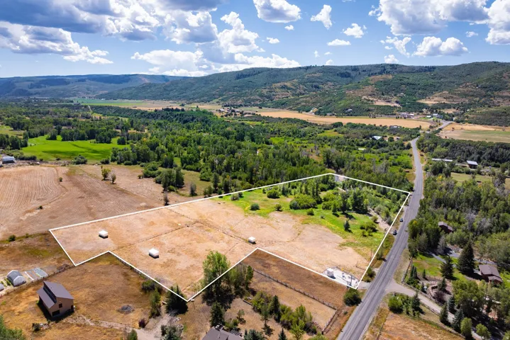 Expansive rural property featuring an open field, mature trees, and direct road frontage