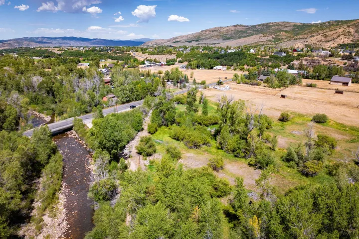 Expansive landscape featuring a natural river, mature trees, a paved road, and distant mountain ranges