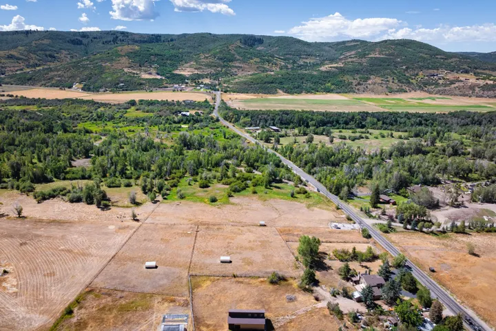 Expansive rural property featuring a paved road, mature trees, and mountainous topography