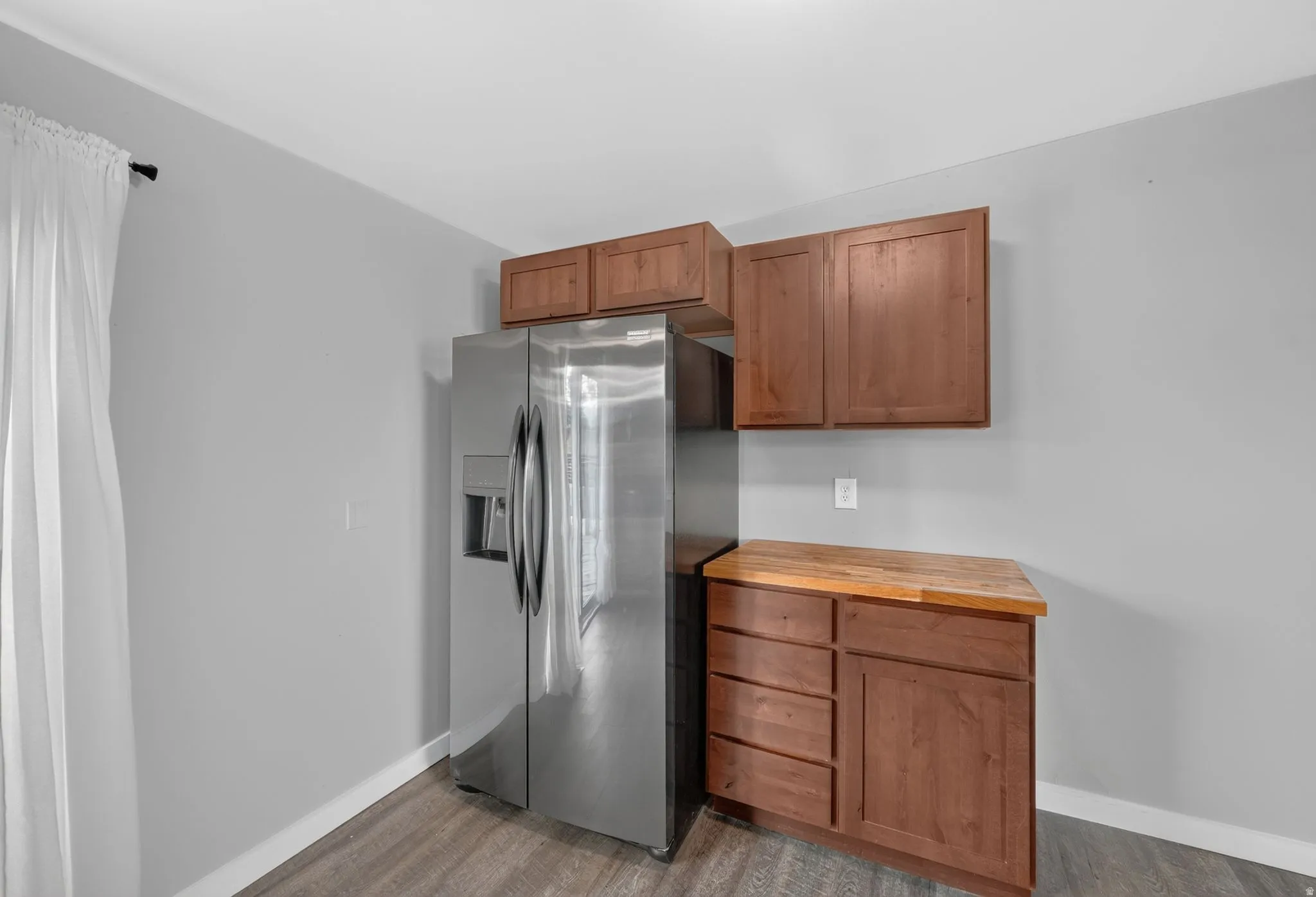 Stainless steel side-by-side refrigerator, wood-finish cabinetry, wood-finish countertop, and wood-finish flooring