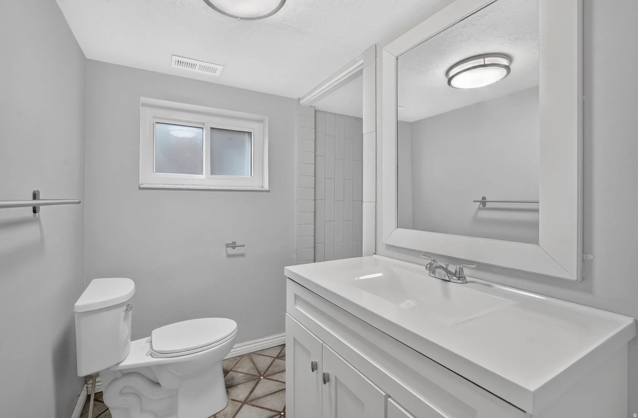 White vanity with integrated sink, chrome faucet, framed mirror, and geometric-patterned floor tiling