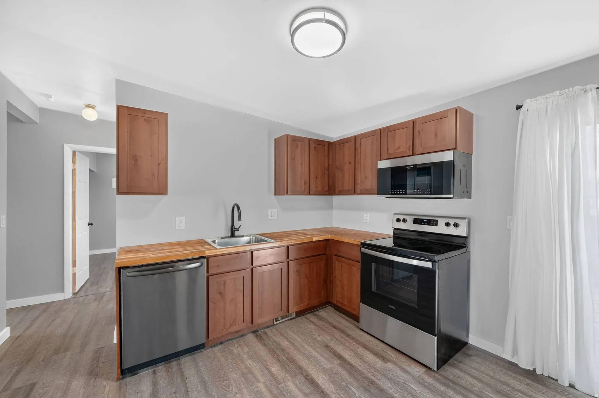 Kitchen featuring wood-finish flooring, wood-finish cabinetry, stainless steel dishwasher, stainless steel range, and stainless steel microwave