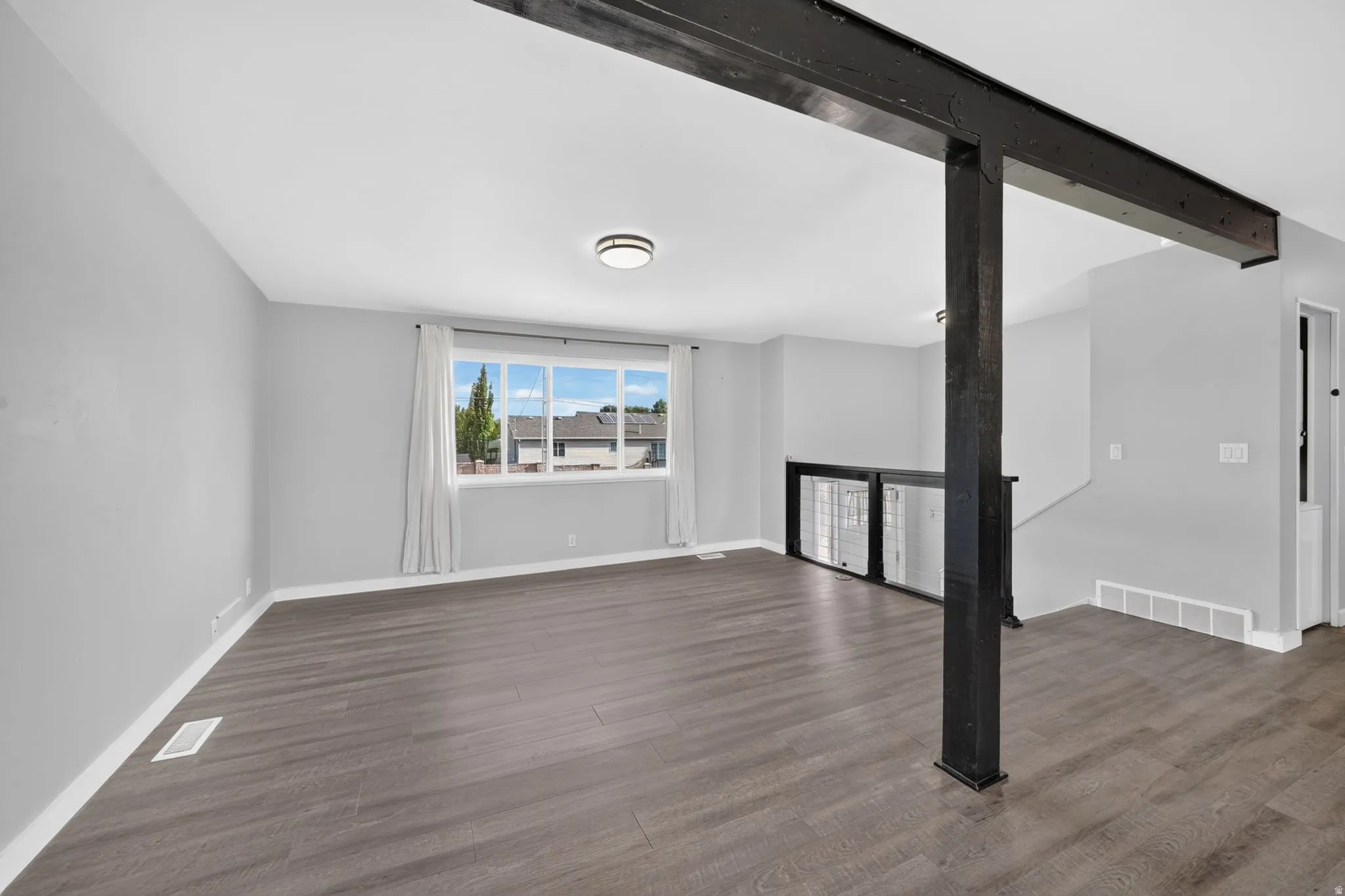Expansive room featuring wood-finish flooring, a large window, a ceiling-mounted light fixture, and a structural beam