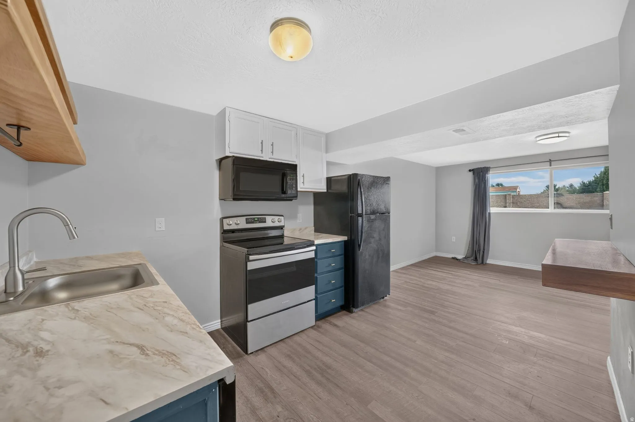 Integrated kitchen featuring a stainless steel sink, wood-finish flooring, and a window providing natural light