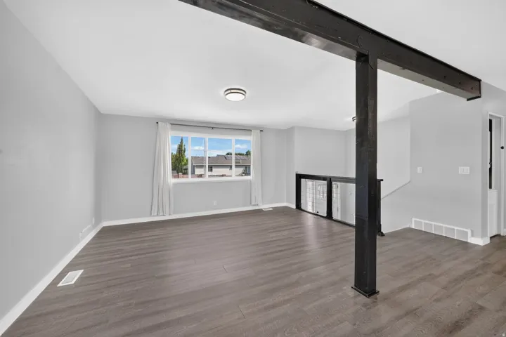 Expansive room featuring wood-finish flooring, a large window, a ceiling-mounted light fixture, and a structural beam