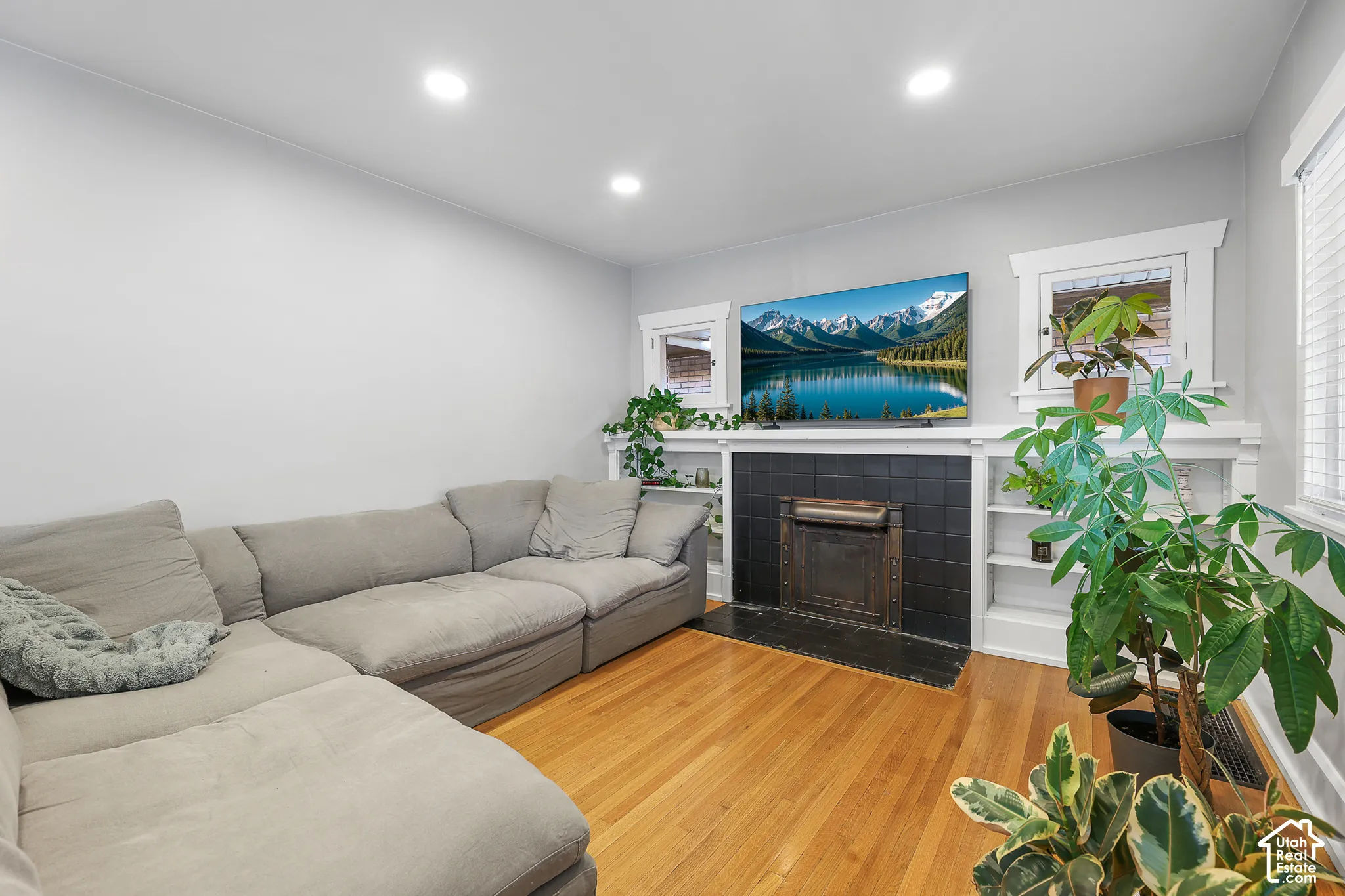 Newly installed recessed lighting, wood flooring, black tile fireplace surround, and built-in shelving