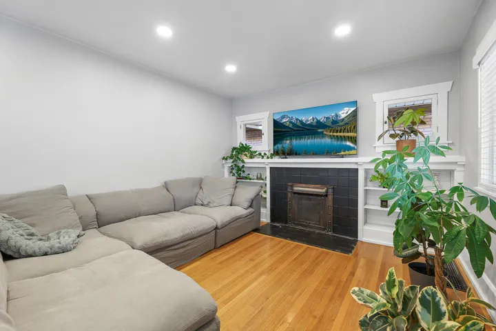 Newly installed recessed lighting, wood flooring, black tile fireplace surround, and built-in shelving