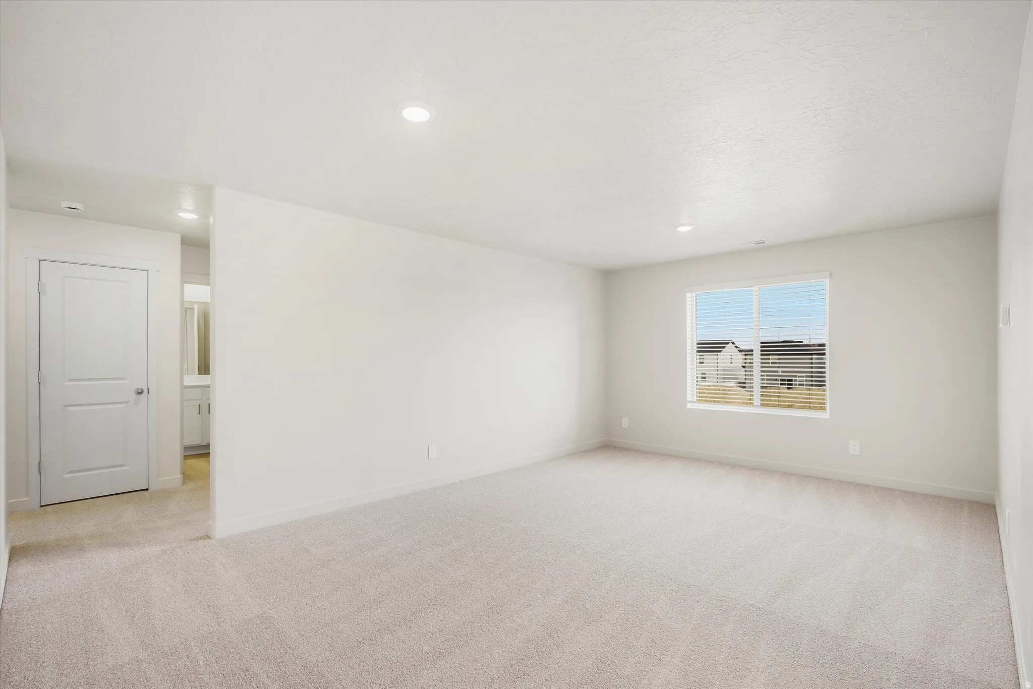 Spacious room with carpet flooring, a large window, recessed lighting, and a neutral color palette