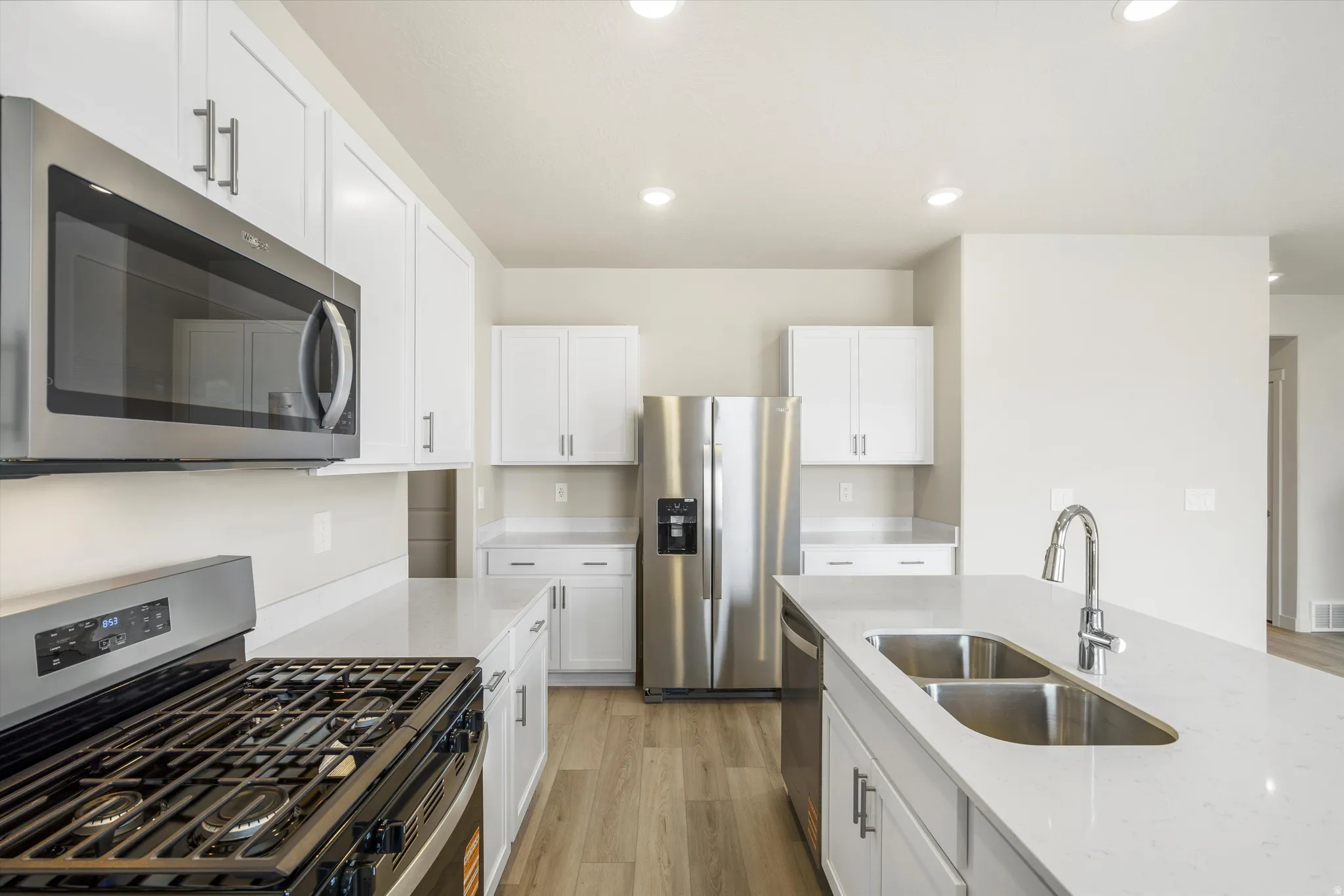 White cabinetry, stainless steel appliances, dual basin undermount sink, light-toned countertops, and wood-finish flooring