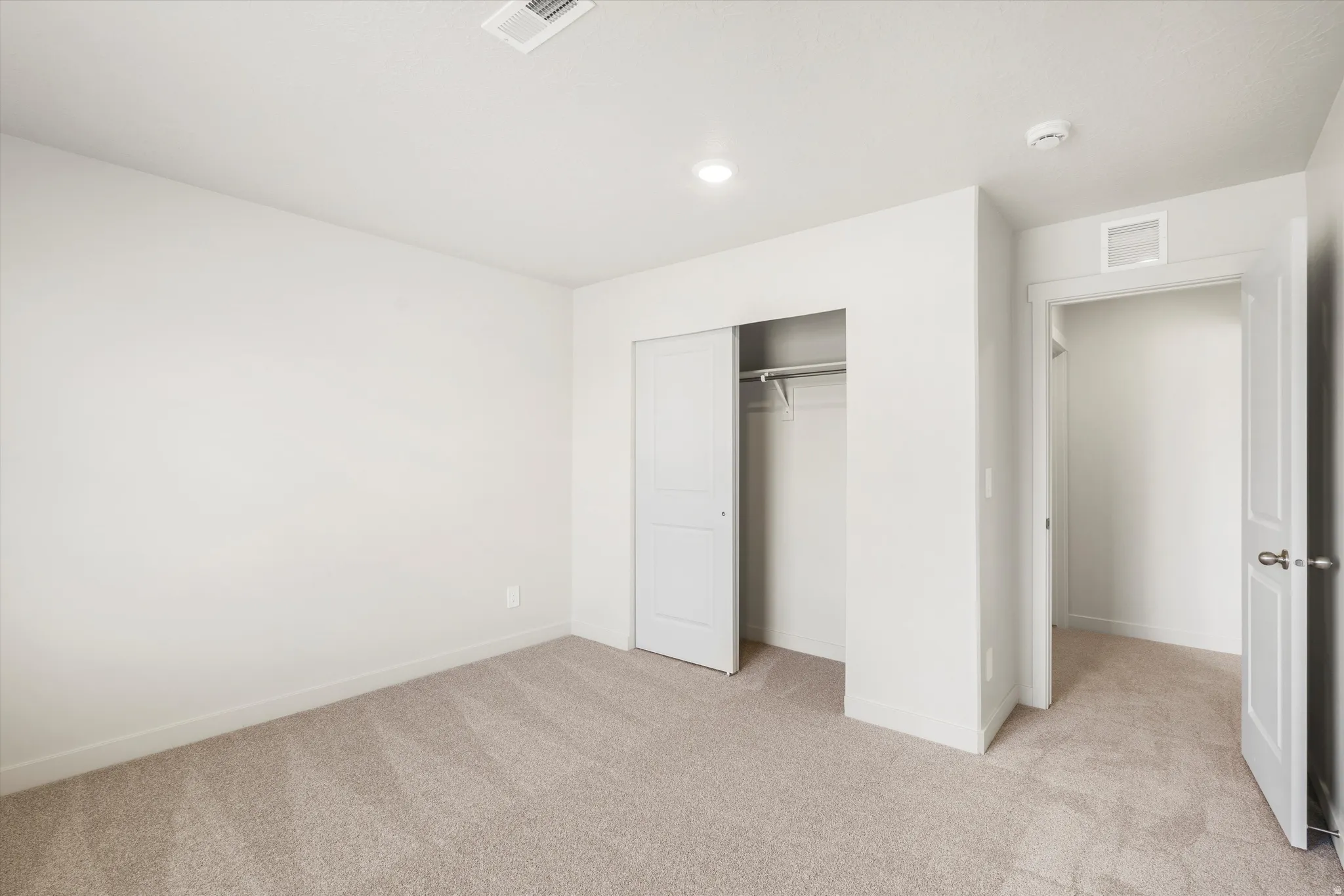 Neutral-toned carpeting, white walls, recessed lighting, white sliding closet doors, and an open doorway