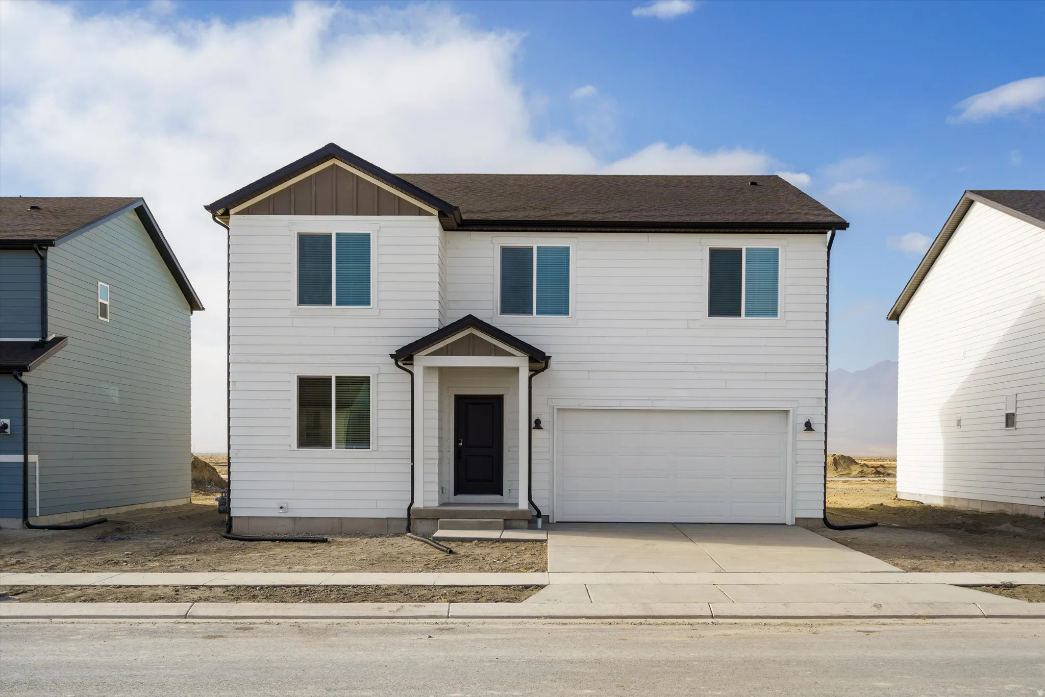 Two-story white siding residence featuring a dark roof, attached garage, and a covered entry porch