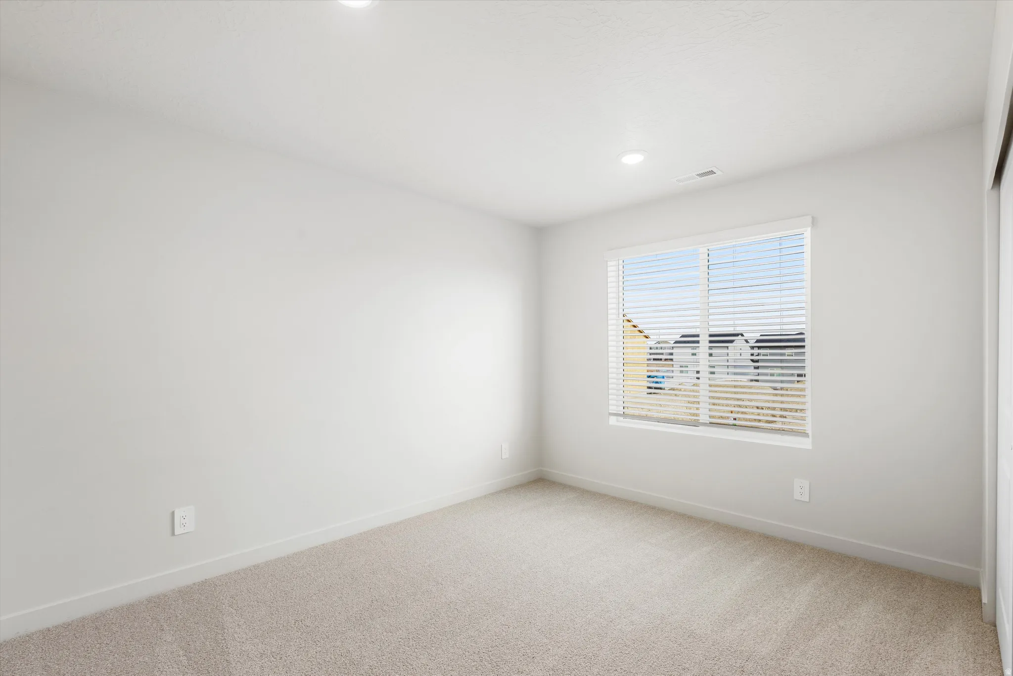 Recessed ceiling lighting, a window with horizontal blinds, and neutral carpeting
