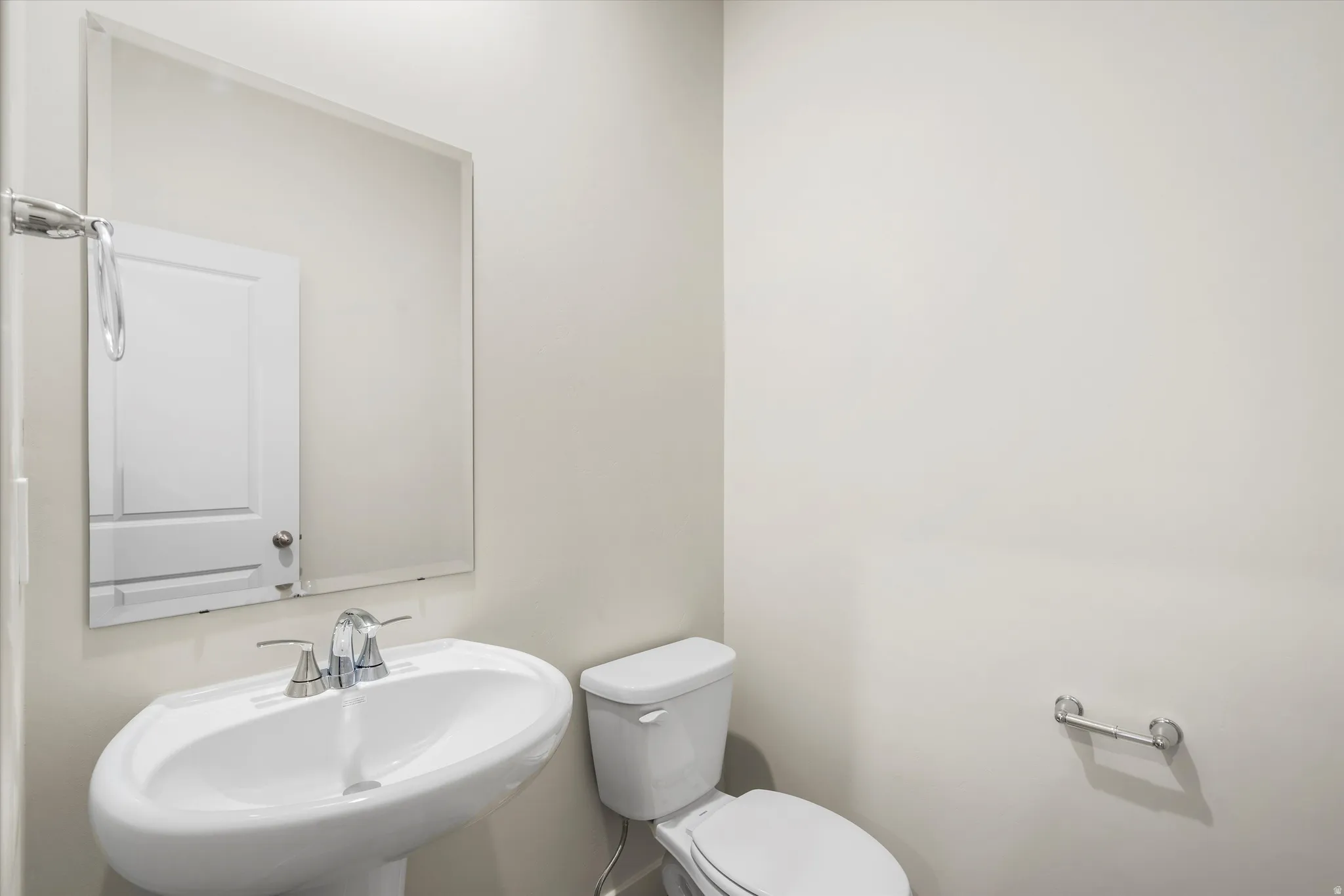 Pedestal sink with chrome faucet, wall-mounted mirror, and white toilet