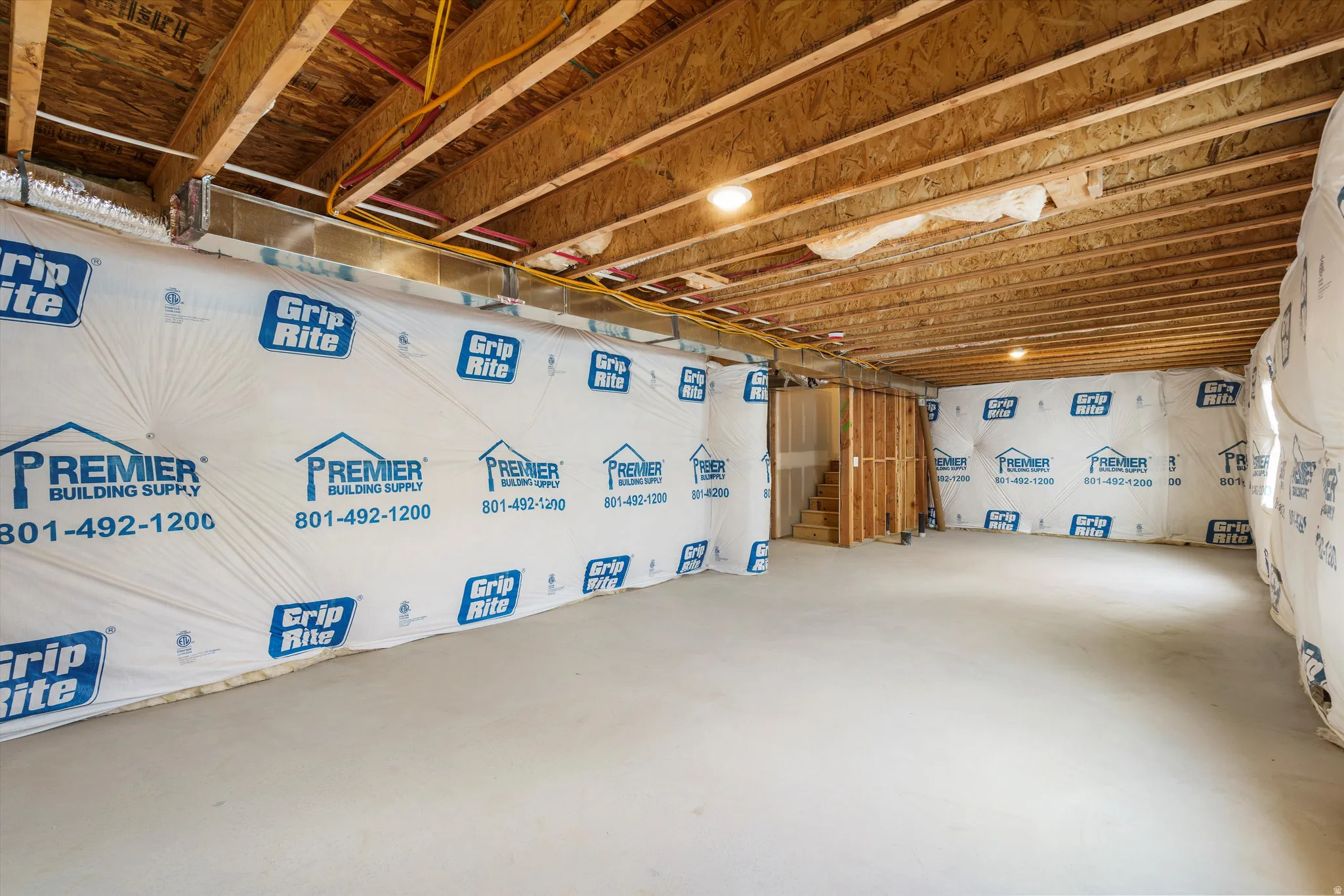 Unfinished basement with exposed wood joists and subflooring, concrete flooring, and partial wall framing