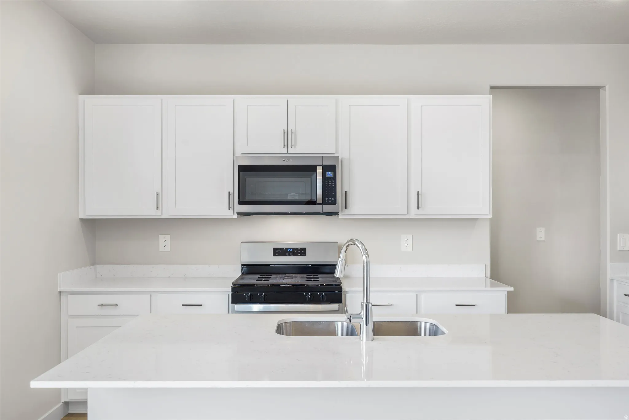 Kitchen featuring white cabinetry, stainless steel microwave, gas range, and a dual-basin sink with a gooseneck faucet