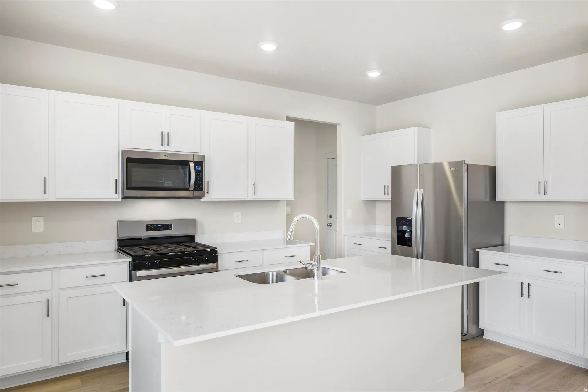 Contemporary kitchen featuring white cabinetry, stainless steel appliances, a center island with sink, quartz countertops, and wood-finish flooring