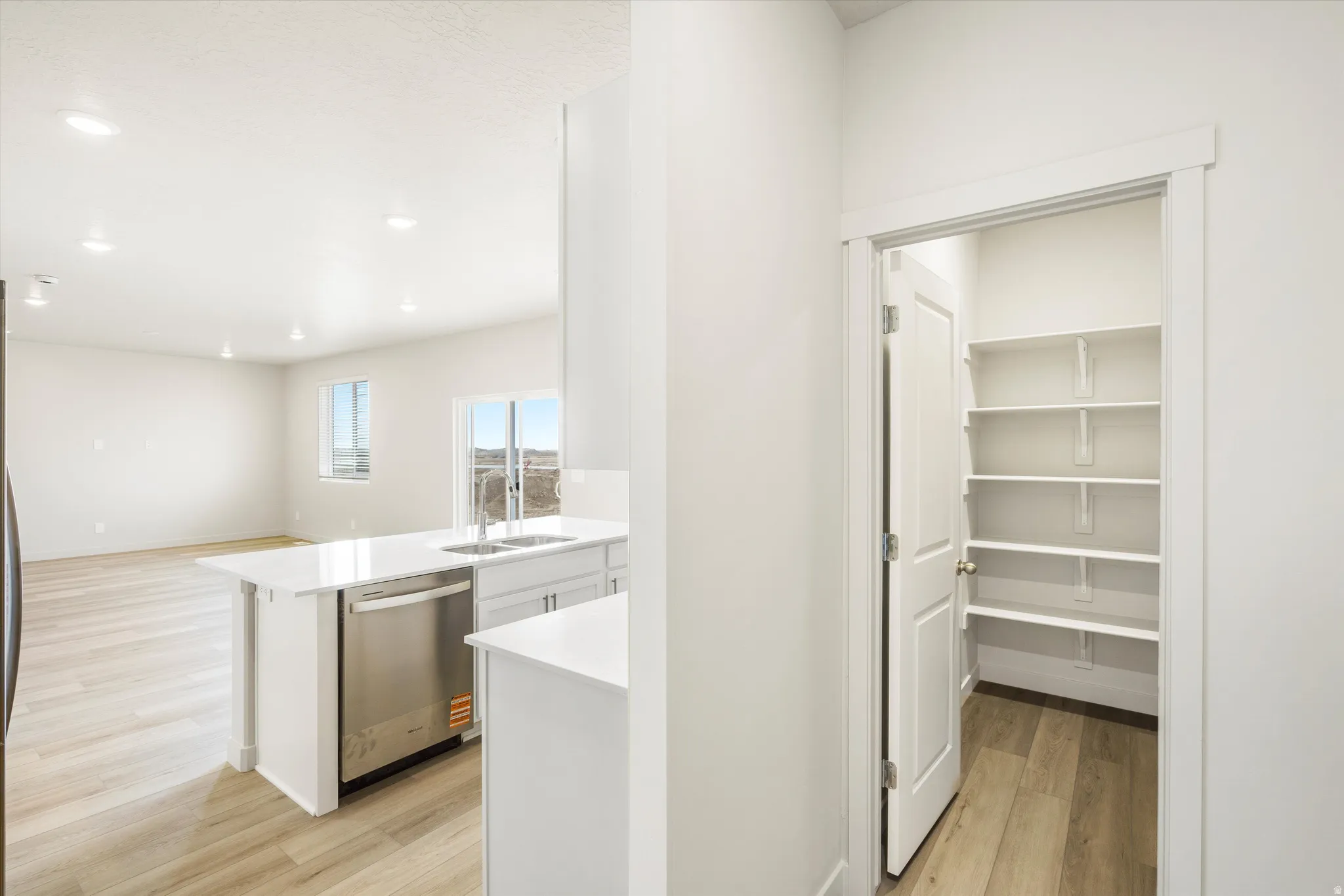 Kitchen island with integrated sink, stainless steel dishwasher, wood-finish flooring, and recessed lighting