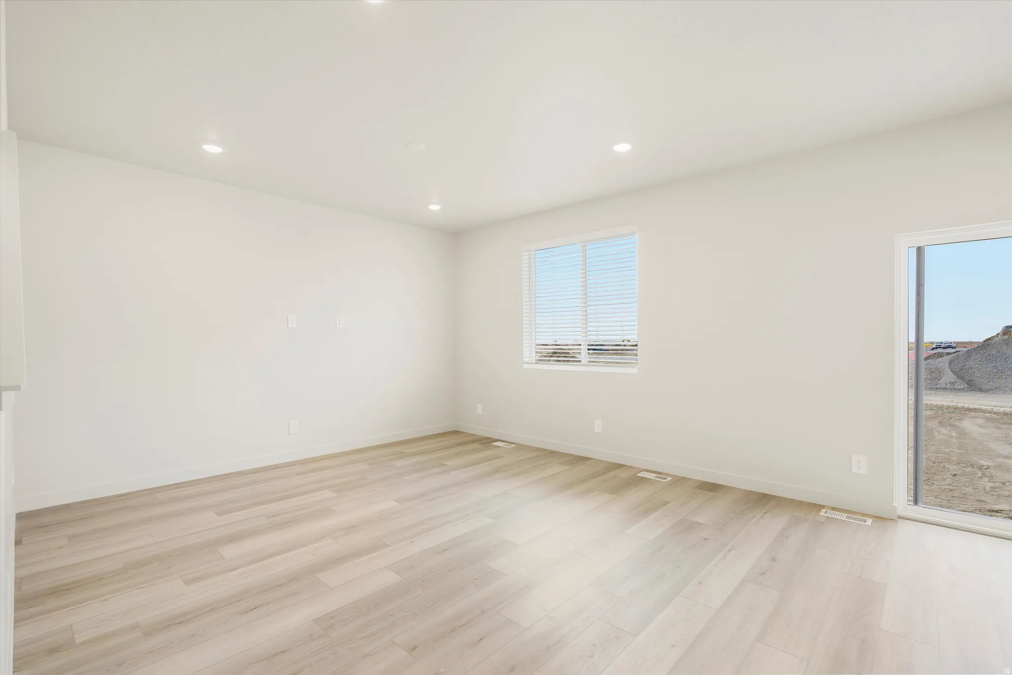 Recessed lighting, light-toned wood-finish flooring, white walls, double-pane window, and a glass sliding door