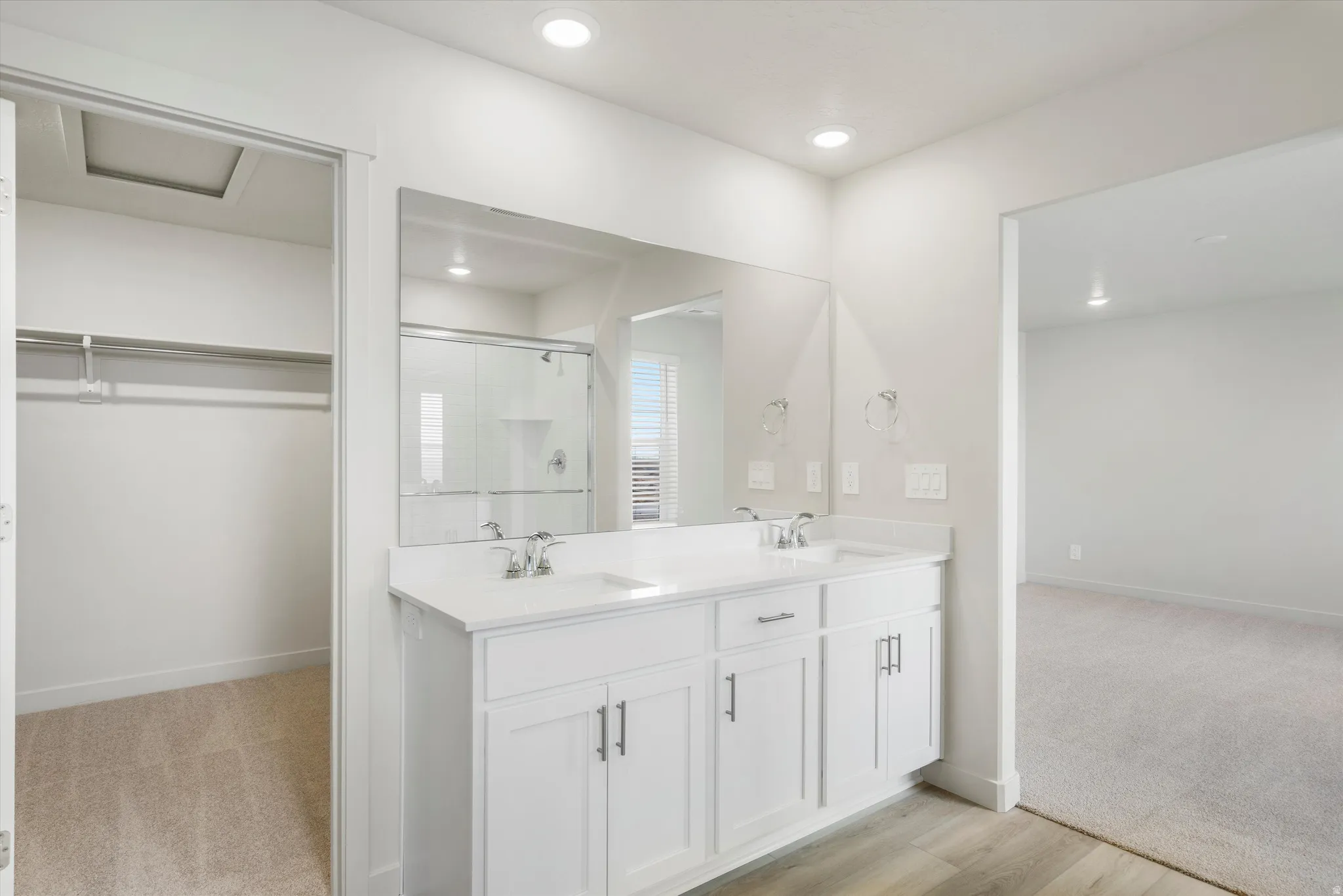 Double vanity with integrated sinks, full-width mirror, and wood-finish flooring