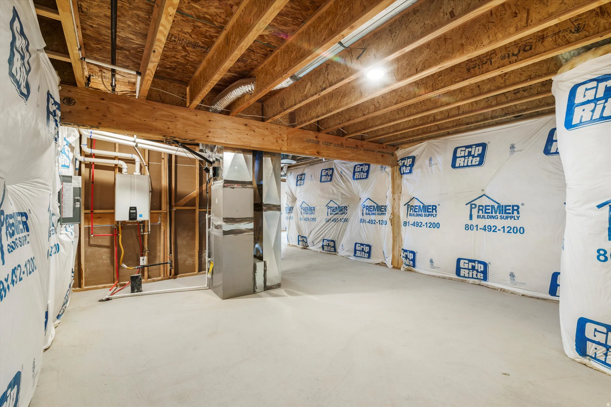 Unfinished basement space featuring exposed wood joists and subflooring, a tankless water heater, and a concrete floor