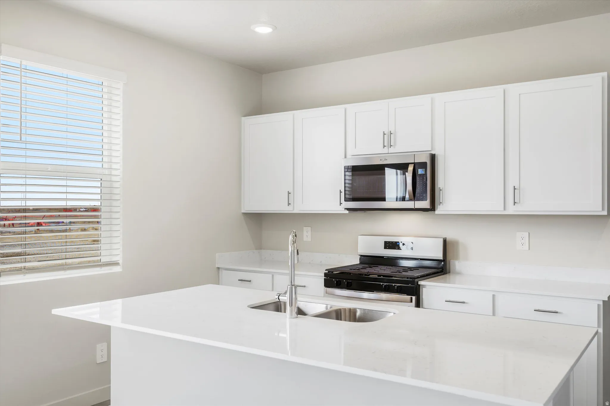 Kitchen featuring white cabinetry, stainless steel appliances, a center island with a double basin sink, and solid surface countertops