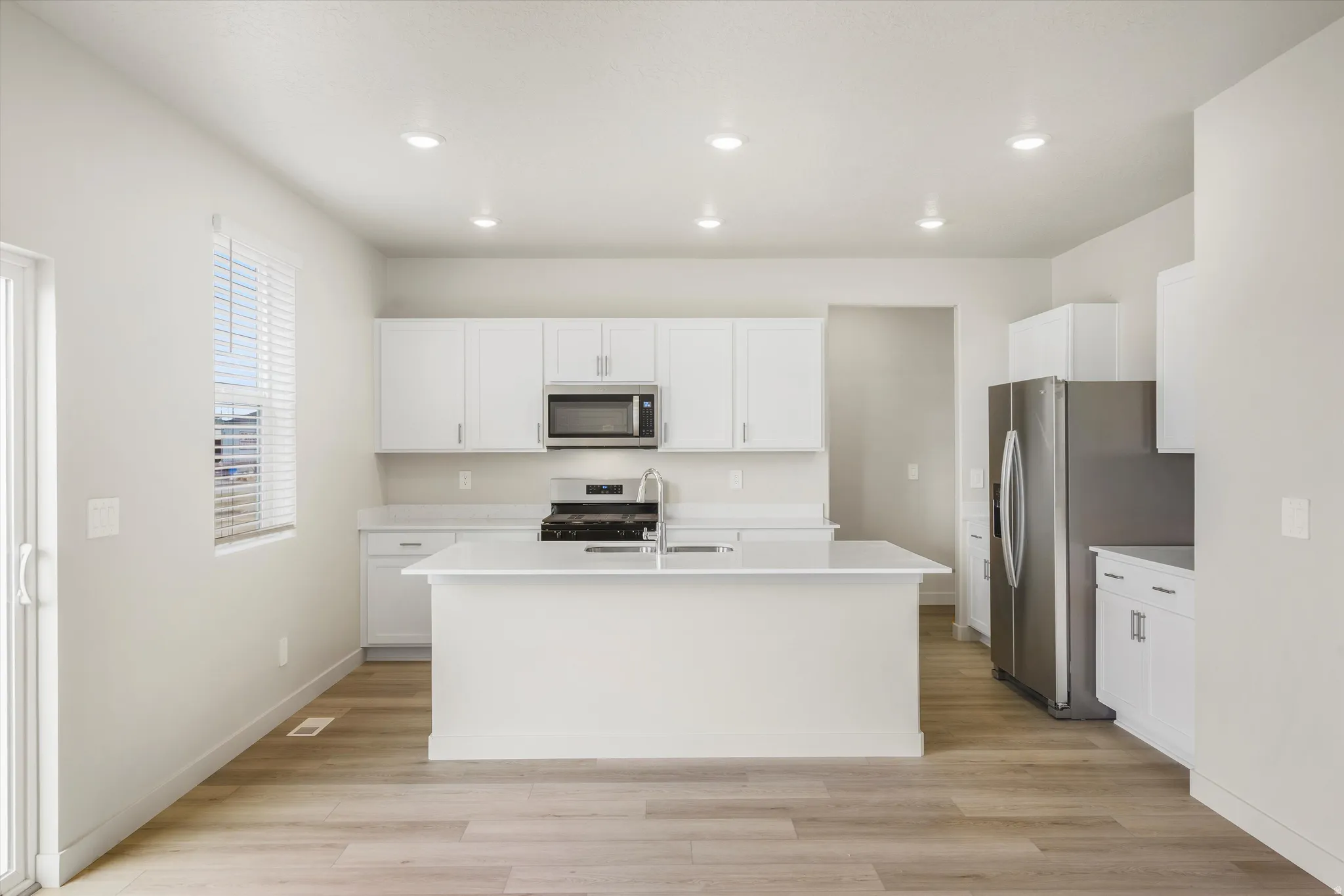 Modern kitchen featuring a central island, white cabinetry, stainless steel appliances, and wood-finish flooring