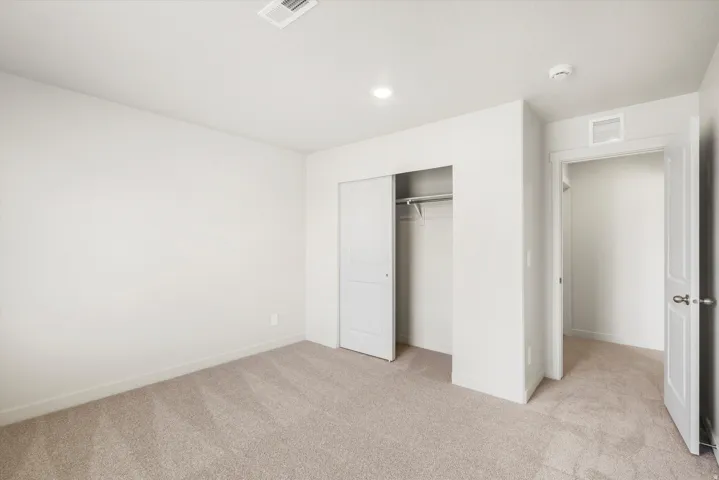Neutral-toned carpeting, white walls, recessed lighting, white sliding closet doors, and an open doorway