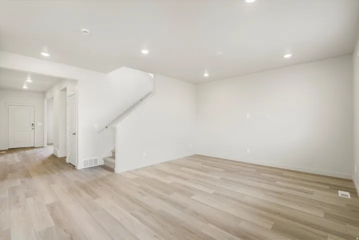 Spacious interior with wood-finish flooring, recessed lighting, and a staircase with carpeted treads