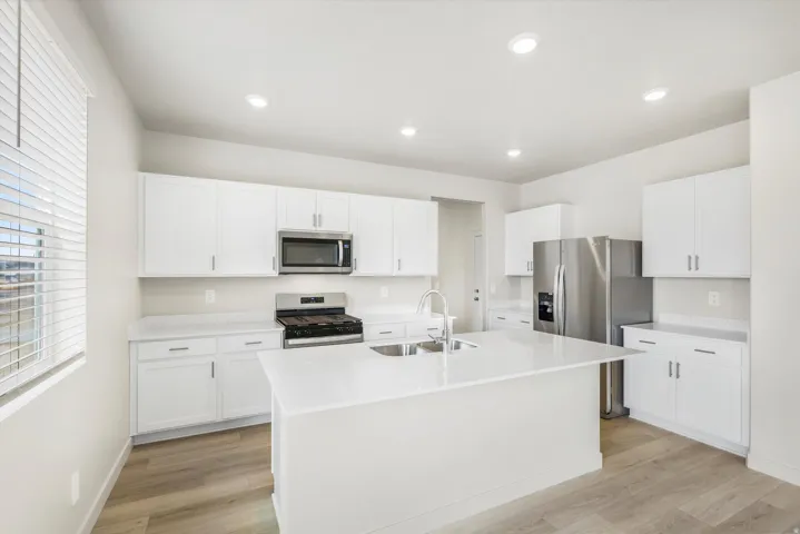 White cabinetry, stainless steel appliances, a center island with sink, recessed lighting, and wood-finish flooring