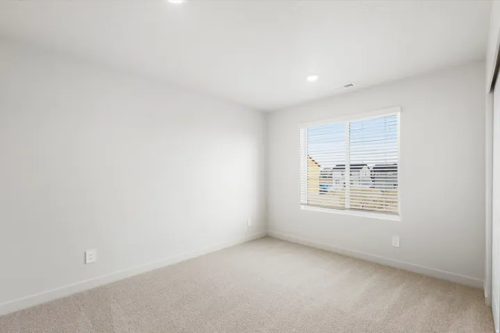 Recessed ceiling lighting, a window with horizontal blinds, and neutral carpeting