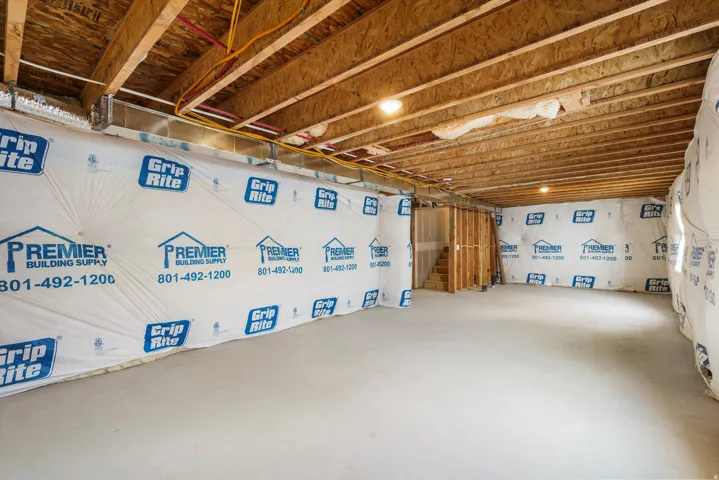 Unfinished basement with exposed wood joists and subflooring, concrete flooring, and partial wall framing