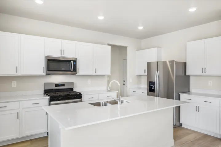 Contemporary kitchen featuring white cabinetry, stainless steel appliances, a center island with sink, quartz countertops, and wood-finish flooring