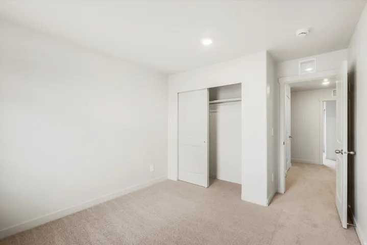 Plush carpet flooring, recessed lighting, white walls, and a built-in closet with sliding doors