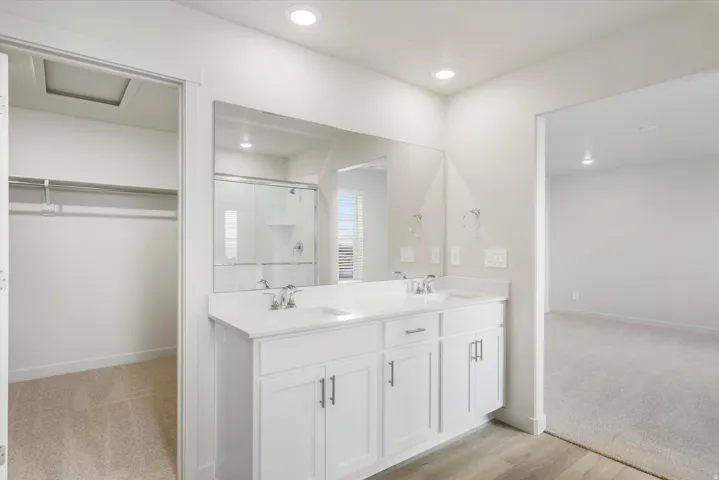 Double vanity with integrated sinks, full-width mirror, and wood-finish flooring