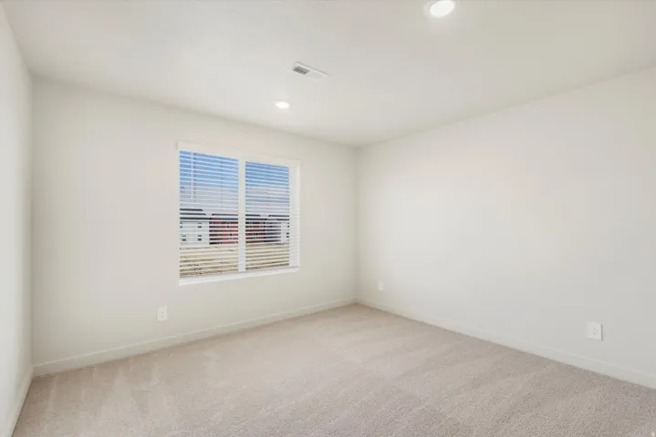 Recessed lighting and a window with blinds illuminate this carpeted room