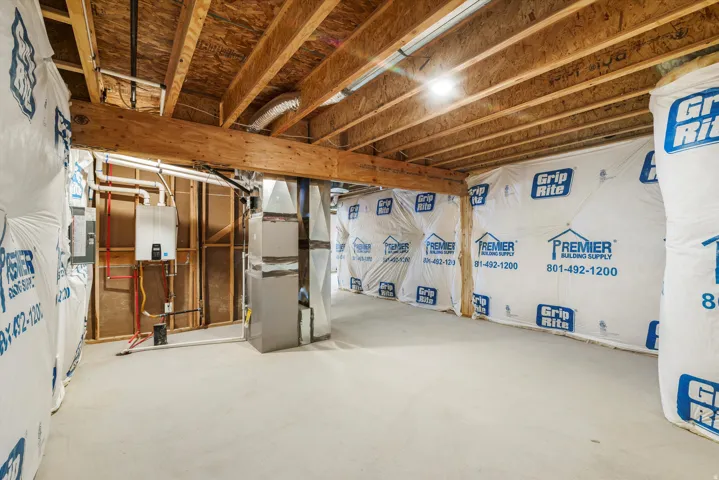 Unfinished basement space featuring exposed wood joists and subflooring, a tankless water heater, and a concrete floor